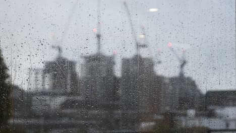 Rain-Falling-down-on-Window-With-Blurred-Construction-Cranes-In-Background