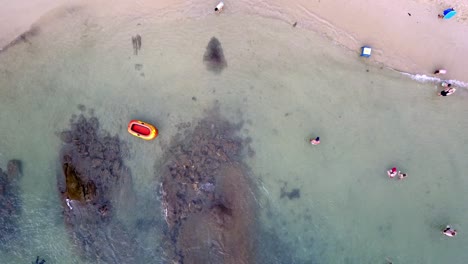 Aerial-top-down-shot-of-people-relaxing-at-the-beach-and-an-empty-inflatable-boat-on-the-water