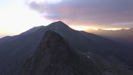 Zerklüfteter-Berggipfel-Und-Schmaler-Grat-Zum-Gipfel-Mit-Dramatischem-Himmel-Und-Goldenen-Lichtstrahlen,-Die-In-Der-Ferne-über-Den-Himmel-Streifen
