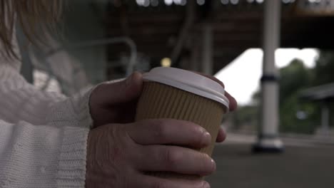 Hände-Halten-Kaffee-Zum-Mitnehmen,-Während-Sie-Auf-Dem-Bahnsteig-Warten,-Mittlere-Aufnahme