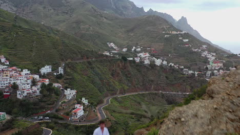 Tipo-De-Pie-Junto-A-Un-Coche,-Volando-Un-Dron-Sobre-Un-Valle-De-Montaña,-Tenerife,-España