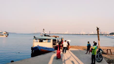 A-small-ferryboat-parked-or-docked-on-jetty-and-tourist-moving-into-the-ferry-with-beautiful-Mumbai-city-background-near-a-bay-in-Mumbai