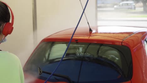 Woman-cleaning-red-car-with-mask-while-listening-to-music,-new-normal