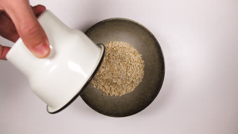 Preparing-Oats-Porridge-For-Healthy-Breakfast-On-Table---Pouring-Rolled-Oats-And-Milk-On-Bowl-And-Then-Put-Black-Spoon