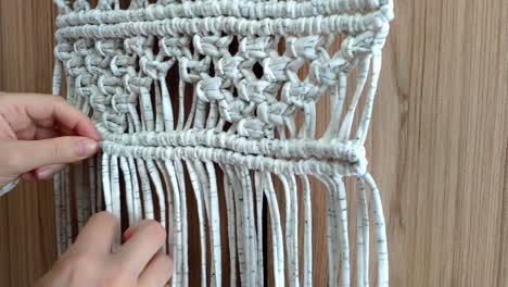 Close-up-of-females-hands-doing-knots-making-a-macrame-decoration-with-white-and-grey-cloth-stripes