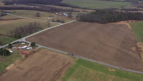 Aerial-pan-shot-of-truck-driving-on-agricultural-road-between-colorful-fields-during-cloudy-day