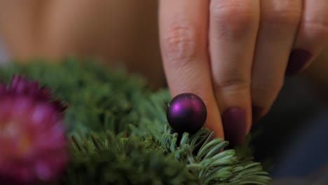 Woman-making-a-fir-Advent-wreath-for-Christmas-Eve-and-decorating-it-with-small-purple-ball,-diy-craft-decoration,-winter-traditions,-seasonal-holidays,-hands-close-up-shot