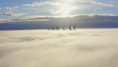 Dolly-back-aerial-shot-over-morning-fog-clouds-from-Canary-Wharf-skyscrapers-sunrise