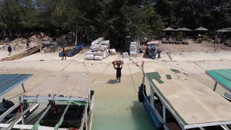 Bundle-Of-Cartons-On-Man's-Head-For-Loading-Into-Boat---Recycling-Trash-Materials-In-Gili-Trawangan-Island,-Indonesia---drone-pullback