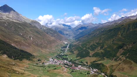 Panning-drone-shot,-looking-down-from-the-Furka-Pass-into-the-Alpine-valley-and-the-town-of-Realp
