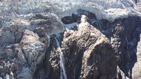 Luftparalaxe-Einer-Großen-Klippe-Mit-Einem-Wasserfall-Aus-Geschmolzenem-Eiswasser-In-Den-Schweizer-Alpen