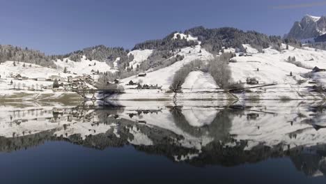 Vuelo-Contra-La-Orilla-De-Un-Lago-Reflectante-En-Los-Alpes-Suizos