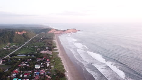 Aerial-View-Of-The-Calm-Sea-Splashing-To-The-Shore-With-Houses-and-Green-Trees-In-Olon-Beach,-Ecuador---Aerial-Shot