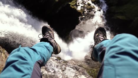 Person-sitting-above-a-beautiful-waterfall,-slow-motion-shot-at-day-time-of-hiker-in-Norway,-Europe