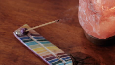 Bursting-smoke-incense-on-a-multicolored-holder-besides-a-pink-salt-lamp-over-a-wooden-table