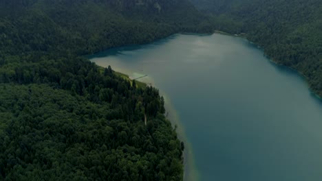 Flying-over-a-beautiful-lake-at-a-forrest-sourroundet-by-mountains,-camera-tilting-up---cinematic-aerial-drone-shot