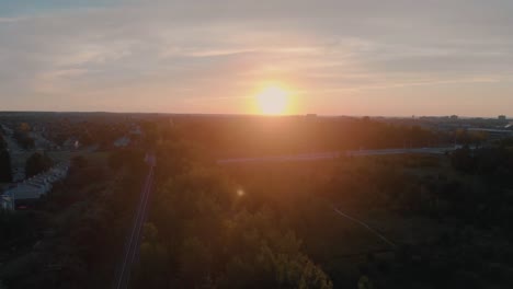 Slow-scenic-aerial-flight-over-train-tracks-outside-nepean-city,-ontario-at-sunrise-with-the-sun-shining-over-the-hill-and-trees