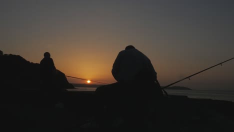 Artistic-silhouette-of-fishermen-casting-their-rods-at-sunrise,-early-bird-catches-the-worm-concept