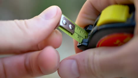 Close-up-of-a-construction-worker-pulling-out-a-yellow-tape-measure-to-check-the-dimensions-for-a-lumber-cut-on-a-jobsite