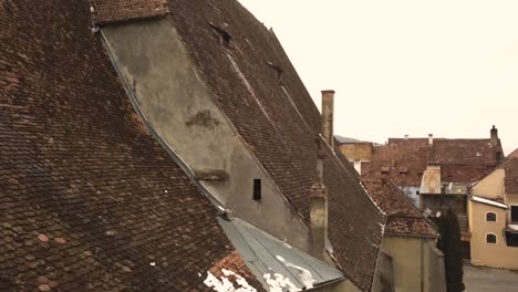 A-drone-shot,-with-a-slant-motion,-capturing-the-rooftop,-of-a-vintage-architechture,-with-some-residual-snow-on-it,-in-the-city-of-Sighisoara-on-an-afternoon