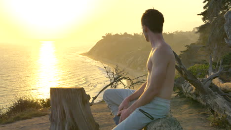 Young-attractive-shirtless-man-resting-after-a-fitness-workout-on-the-edge-of-a-cliff-above-the-Pacific-ocean-during-a-golden-sunset-in-Santa-Barbara,-California