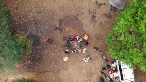Aerial-reveal-shot-of-young-people-around-a-campfire-roasting-hotdogs-while-camping-in-the-forest