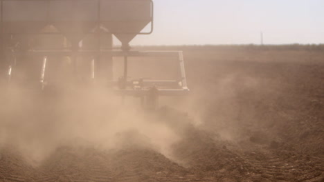 Close-up-of-a-Plow-tilling-the-field-while-its-dry-and-kicking-up-a-cloud-of-dust