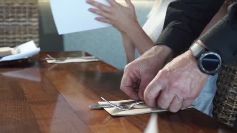 SLOWMO---Male-waiter-putting-cutlery-on-wooden-table-while-young-blond-hair-woman-looking-at-the-menu-in-luxury-restaurant---low-close-up