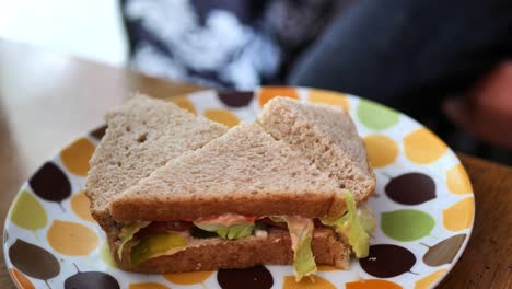Little-kid-with-dirty-hands-picking-up-a-quarter-piece-of-cut-up-sandwich-with-whole-wheat-bread,-pickles,-and-lettuce