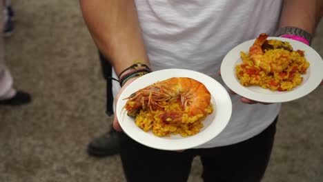 SLOWMO---Man-holding-plate-of-pallea---prawns,-shrimps,-mussels,-rice-and-tomatoes---close-up