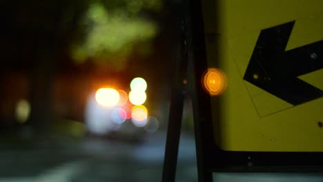 Night-time-road-traffic-sign-pointing-direction-with-traffic-bokeh