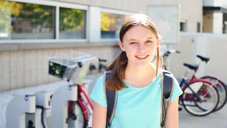 Portrait-of-happy-fifteen-year-old-girl-by-city-bikes