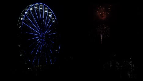 A-ferris-wheel-lights-up-the-sky-with-a-fireworks-show-beside-it-in-the-night-sky