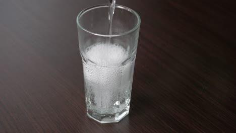 Pouring-transparent-soda-into-a-tall-glass-on-a-wooden-table