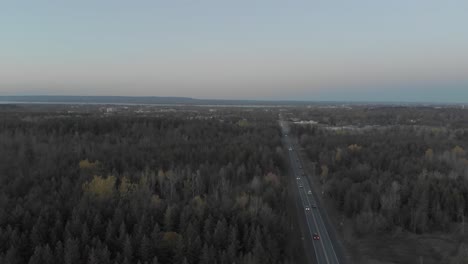 Aerial-footage-moving-to-the-right-over-a-busy-road-just-outside-of-Ottawa,-Ontario-with-the-city-skyline-in-the-distance-and-a-blue-skyline