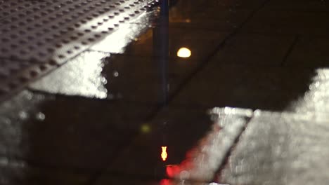 Puddle-reflecting-urban-sidewalk-pedestrian-crossing-lights-change-on-rainy-night
