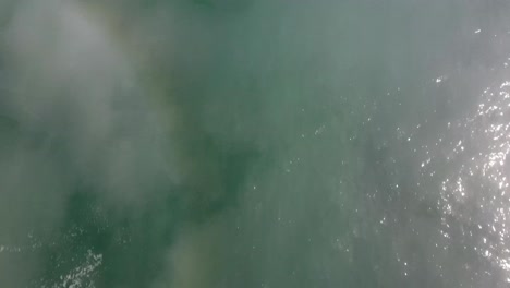 AERIAL:-Ocean-view-with-mist-and-clouds-catching-the-light-and-creating-rainbows