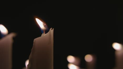 An-extreme-close-up-of-white-candles-lit-with-a-black-background-in-slow-motion