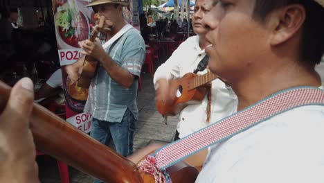 Three-guitar-mariachi-singing-and-playing-their-guitars-outdoors-at-a-festival-in-Merida,-Mexico