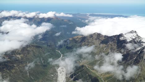 SLOWMO---Aerial-shot-from-plane-scenic-flight-over-west-coast-Fox-Glacier,-Aoraki-Mount-Cook,-National-Park-with-clouds,-snowcapped-rocky-mountains-and-ocean-in-background