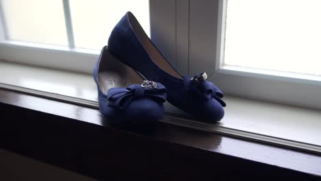Slow-push-in-shot-of-a-bride's-wedding-shoes-in-a-large-window-sill-with-the-rings-resting-on-top