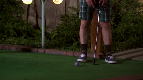 A-close-up-of-a-purple-mini-golf-ball-getting-hit-with-a-club-and-the-shot-is-horrible-and-the-ball-comes-rolling-back-to-the-golfer