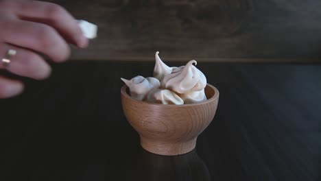 Close-up-on-men's-hand-reaching-for-white-meringue-on-wooden-bowl