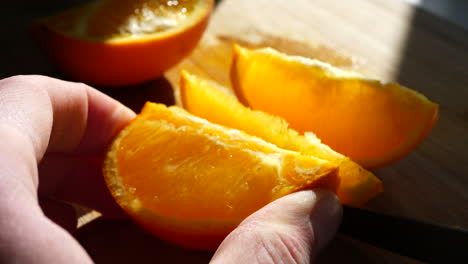 Cutting-a-ripe-orange-fruit-slice-with-a-knife-in-the-sunlight-on-a-cutting-board-for-a-healthy-snack