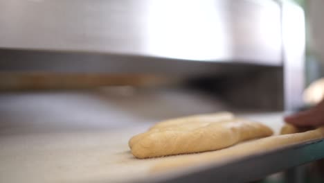 Close-up-making-bread-in-a-bakery-as-a-baker-rolls-out-strands-of-dough-after-they-come-out-of-the-bread-roller