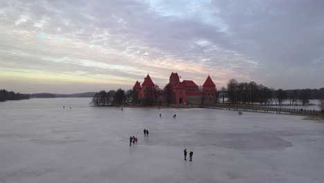 AERIAL:-Flying-Towards-Trakai-Island-Castle-Over-Frozen-Lake-With-People-Walking-on-the-Ice