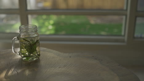 Herbal-tea-glass-is-set-down-on-table-overlooking-garden