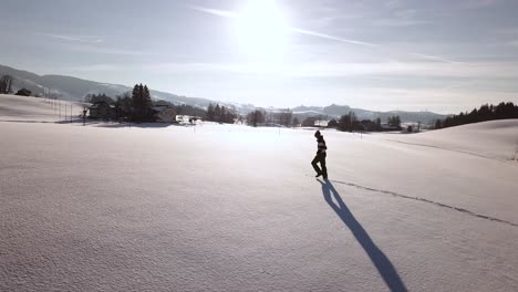 A-young-man-with-winter-clothes-walks-through-a-big-snowy-field-in-Switzerland-while-winter