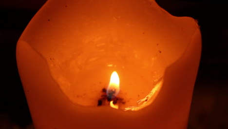 Angled-view-of-a-yellow,-orange-and-red-candle-with-a-litted-shaky-flame-and-melted-wax-on-dark-background