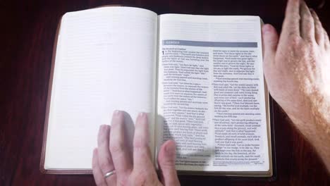 Top-down-shot-opening-up-a-leather-bound-bible-to-the-book-of-Genesis-on-a-wooden-table